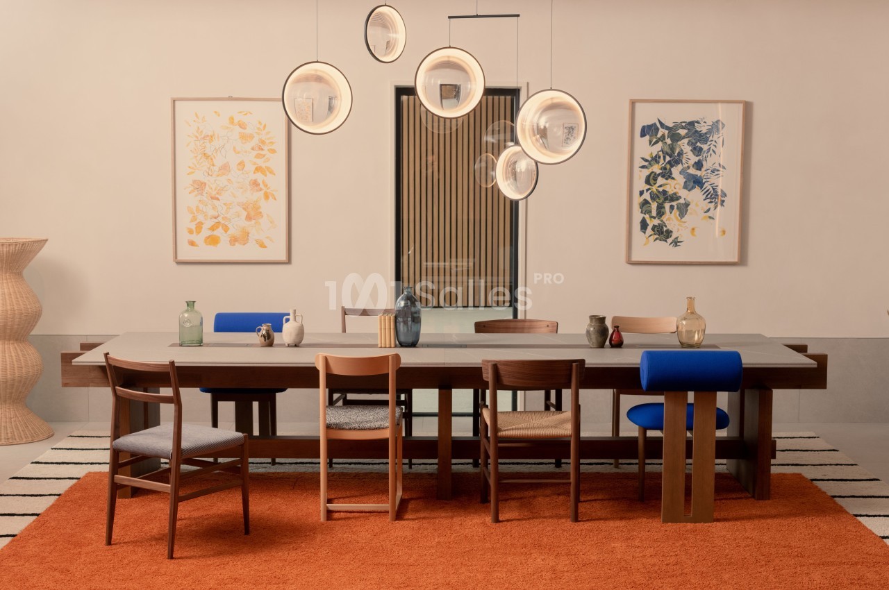 Salle à manger avec table en bois, chaises variées, suspension lumineuse moderne et décorations murales colorées.