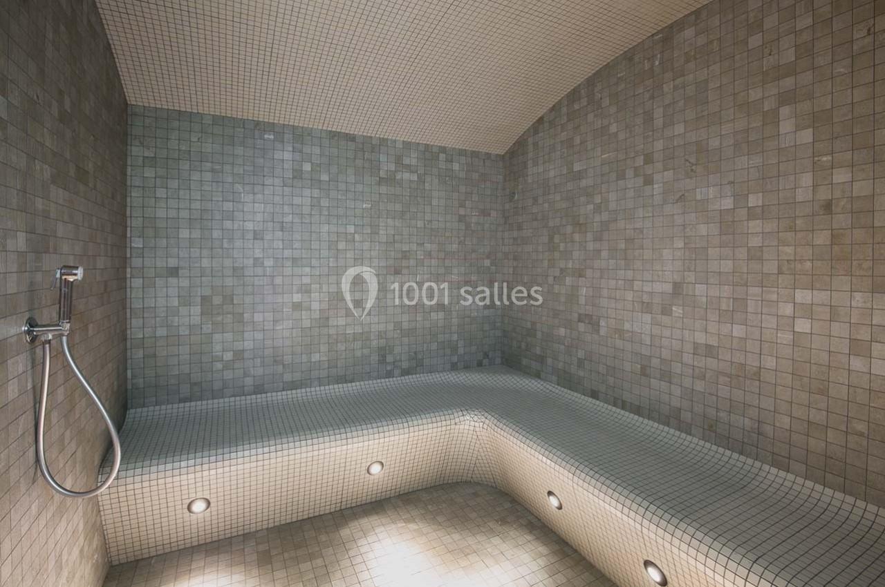 Banc carrelé avec douche murale dans un hammam aux tons clairs et éclairage intégré au sol.