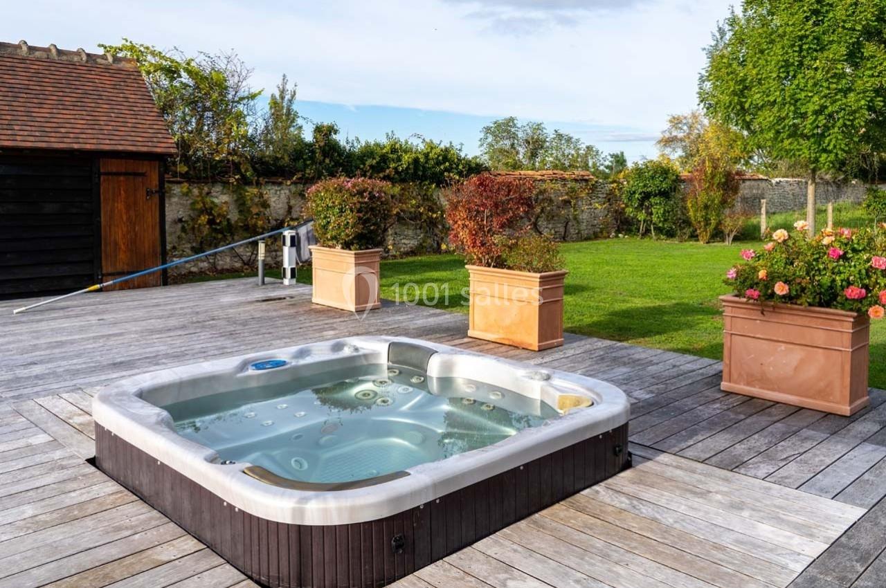 Spa encastré dans une terrasse en bois, entouré de jardinières et d'un jardin avec pelouse et arbres.
