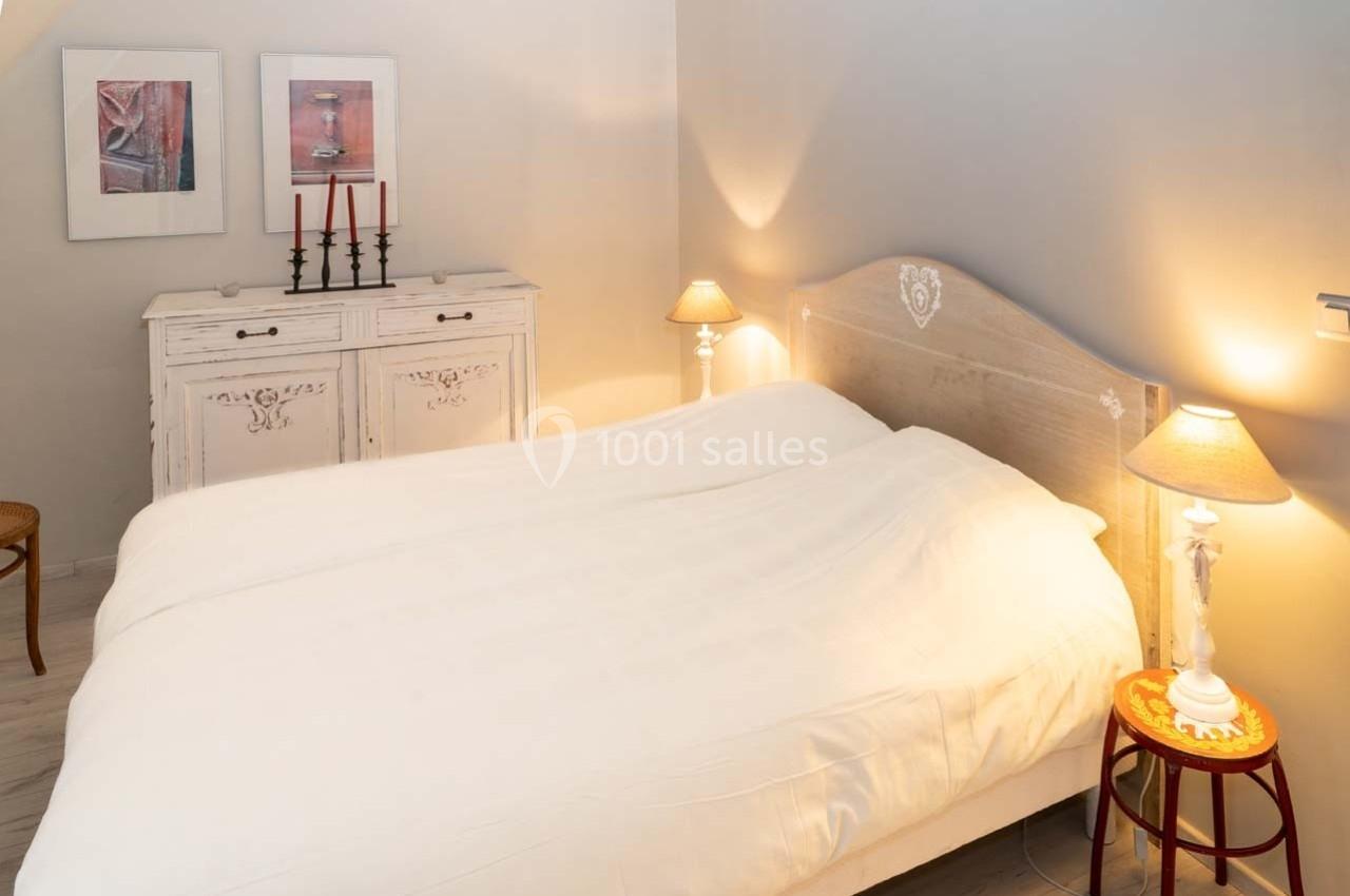 Chambre lumineuse avec un lit double, des lampes de chevet allumées et un meuble blanc décoré de cadres.