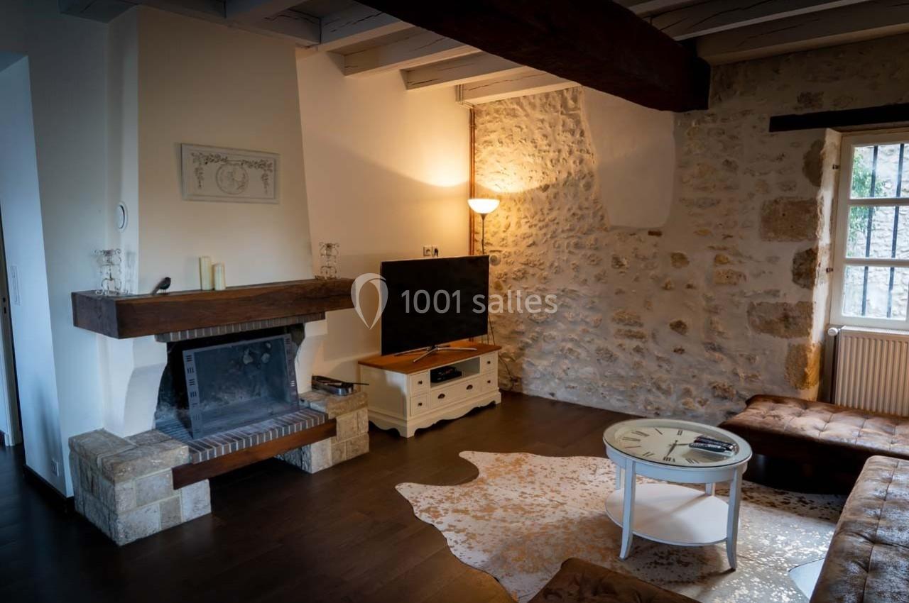 Salon chaleureux avec murs en pierre, cheminée, téléviseur, canapé en cuir et table basse sur tapis clair.