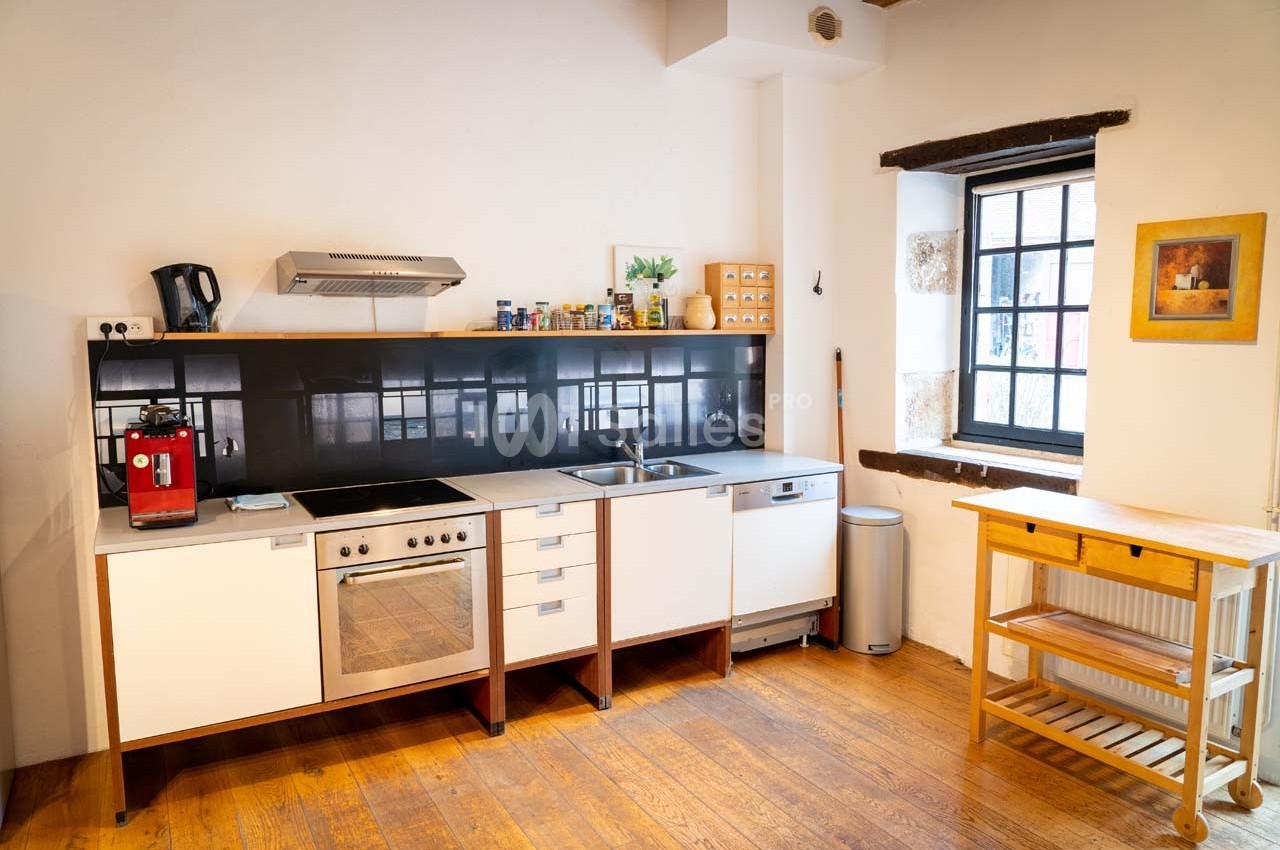 Cuisine lumineuse avec plancher en bois, meubles blancs, électroménagers modernes et fenêtre laissant entrer la lumière…