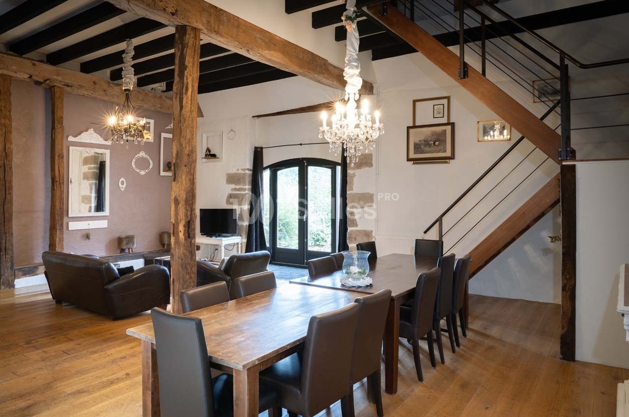 Salle à manger spacieuse avec table en bois, chaises noires, poutres apparentes et escalier en métal.