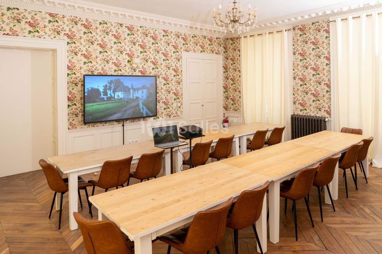 Salle de réunion lumineuse avec tables en bois, chaises en cuir, écran mural et murs ornés de papier peint fleuri.