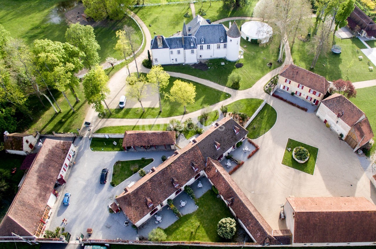 Vue aérienne d'un domaine avec bâtiments en pierre, cour centrale, espaces verts et allées arborées.
