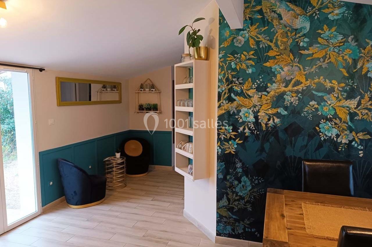 Salle à manger lumineuse avec mur à motifs floraux, table en bois, étagères décoratives et vue sur un jardin.