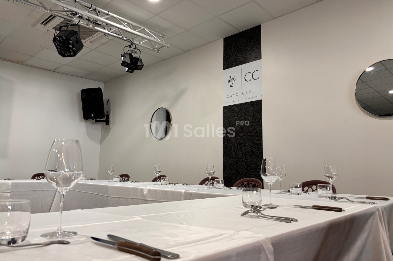 Salle de réception avec tables dressées, nappes blanches, verres et couverts, éclairage suspendu et miroirs muraux.