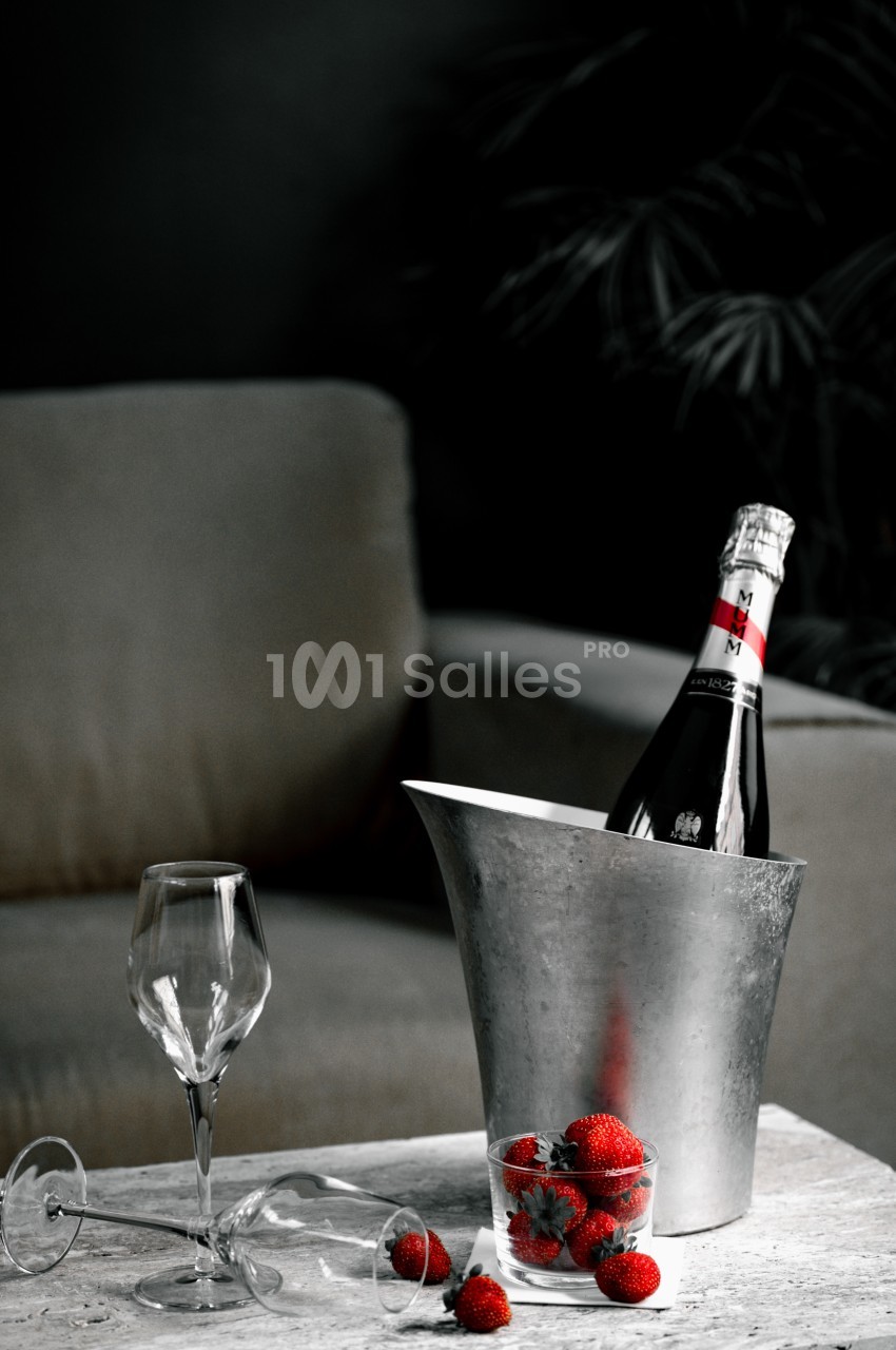 Bouteille de champagne dans un seau à glace, verre vide et fraises sur une table devant un canapé.