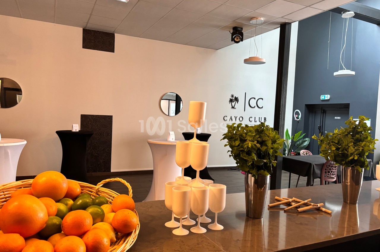 Panier de fruits, verres blancs et décoration végétale sur un comptoir dans un espace intérieur moderne et lumineux.