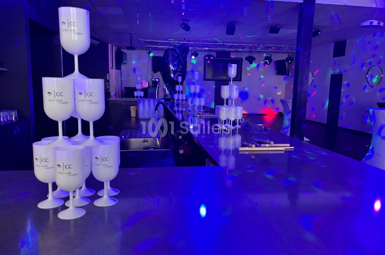 Salle de réception avec comptoir central, gobelets empilés et éclairage coloré créant une ambiance festive.