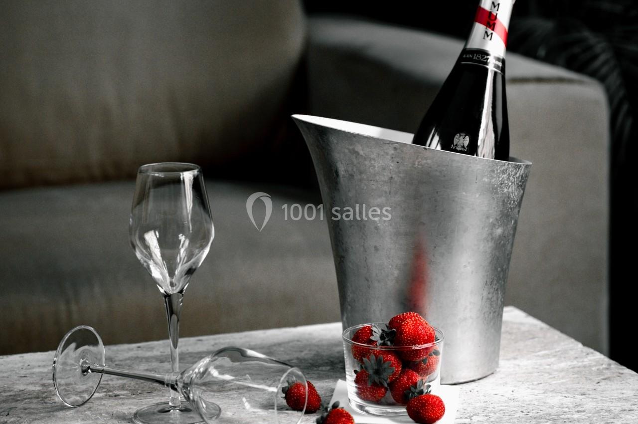 Bouteille de champagne dans un seau en métal, deux verres à pied et des fraises dans un bol sur une table.
