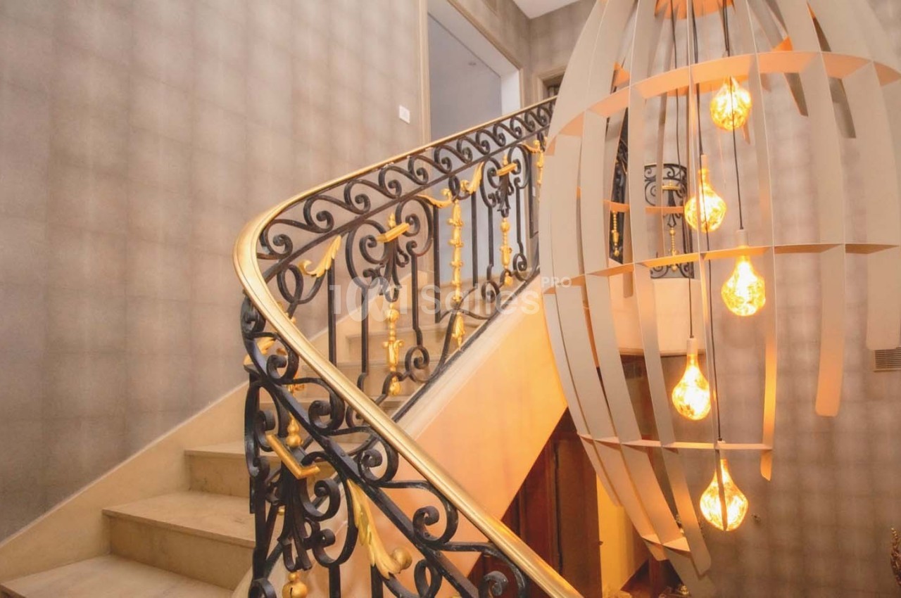 Escalier en marbre avec rampe en fer forgé ornée, éclairé par une suspension moderne avec ampoules apparentes.