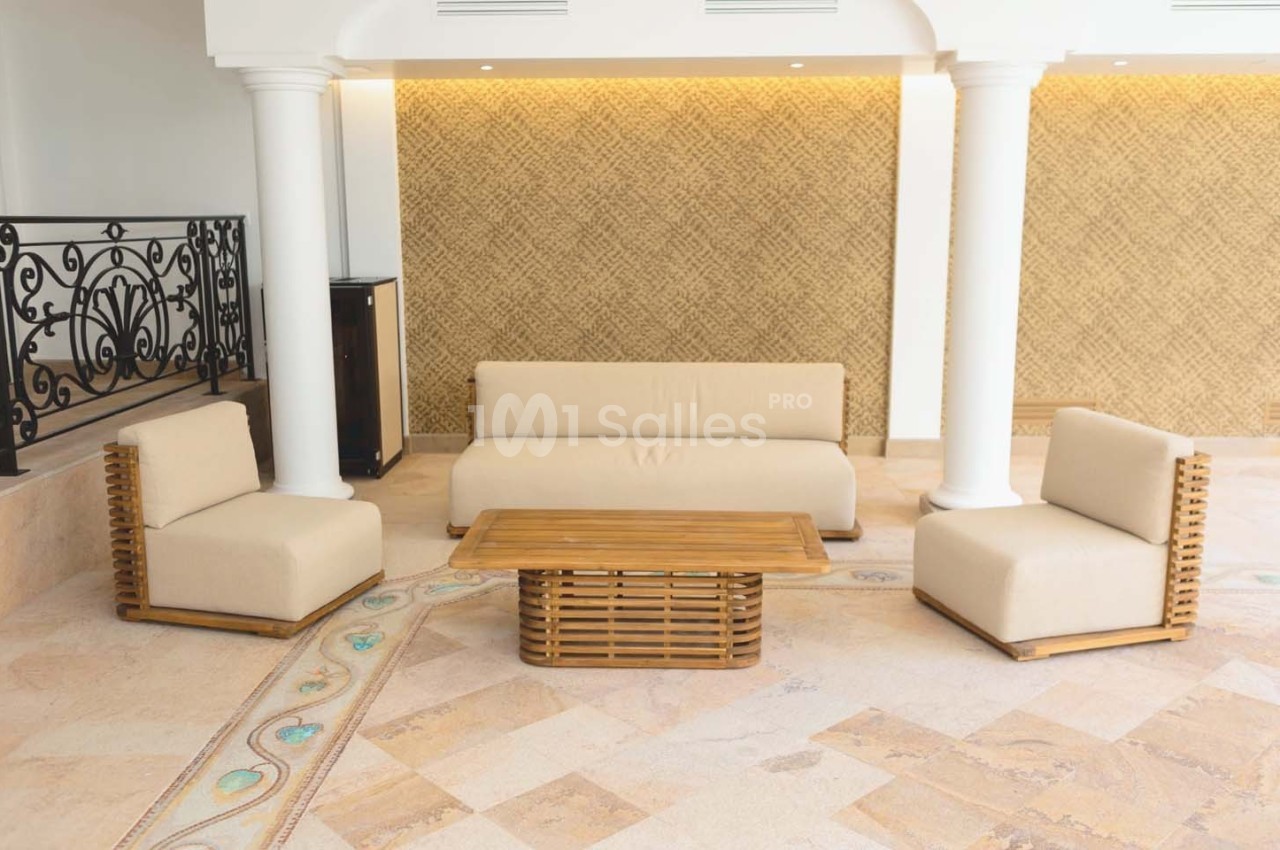Mobilier de salon avec canapé, fauteuils et table basse en bois, disposés sur un sol en pierre dans un espace lumineux.