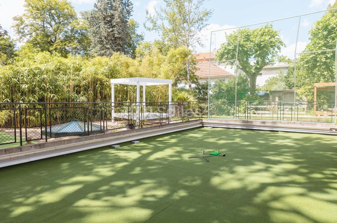Terrain de sport extérieur en gazon synthétique entouré de végétation, avec un équipement posé au centre.