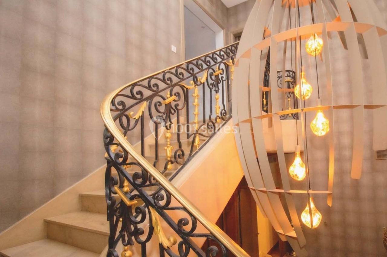 Escalier en colimaçon avec rampe en fer forgé orné, éclairé par un lustre moderne suspendu.