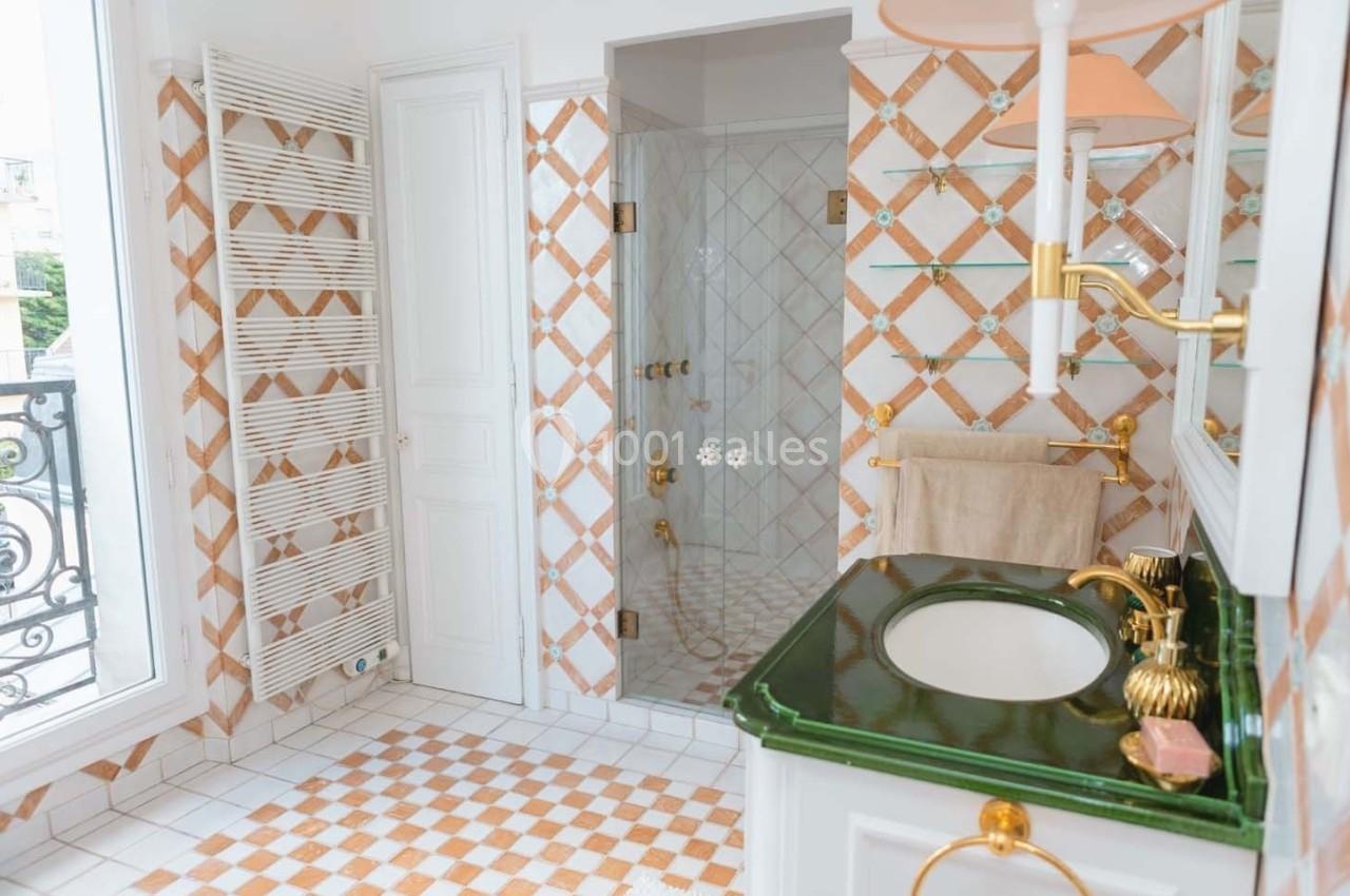 Salle de bain lumineuse avec carrelage à motifs, douche vitrée, lavabo avec plan en marbre vert et sèche-serviettes mural.