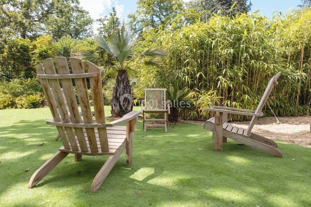Chaises en bois disposées sur une pelouse dans un jardin avec bambous et palmiers en arrière-plan.