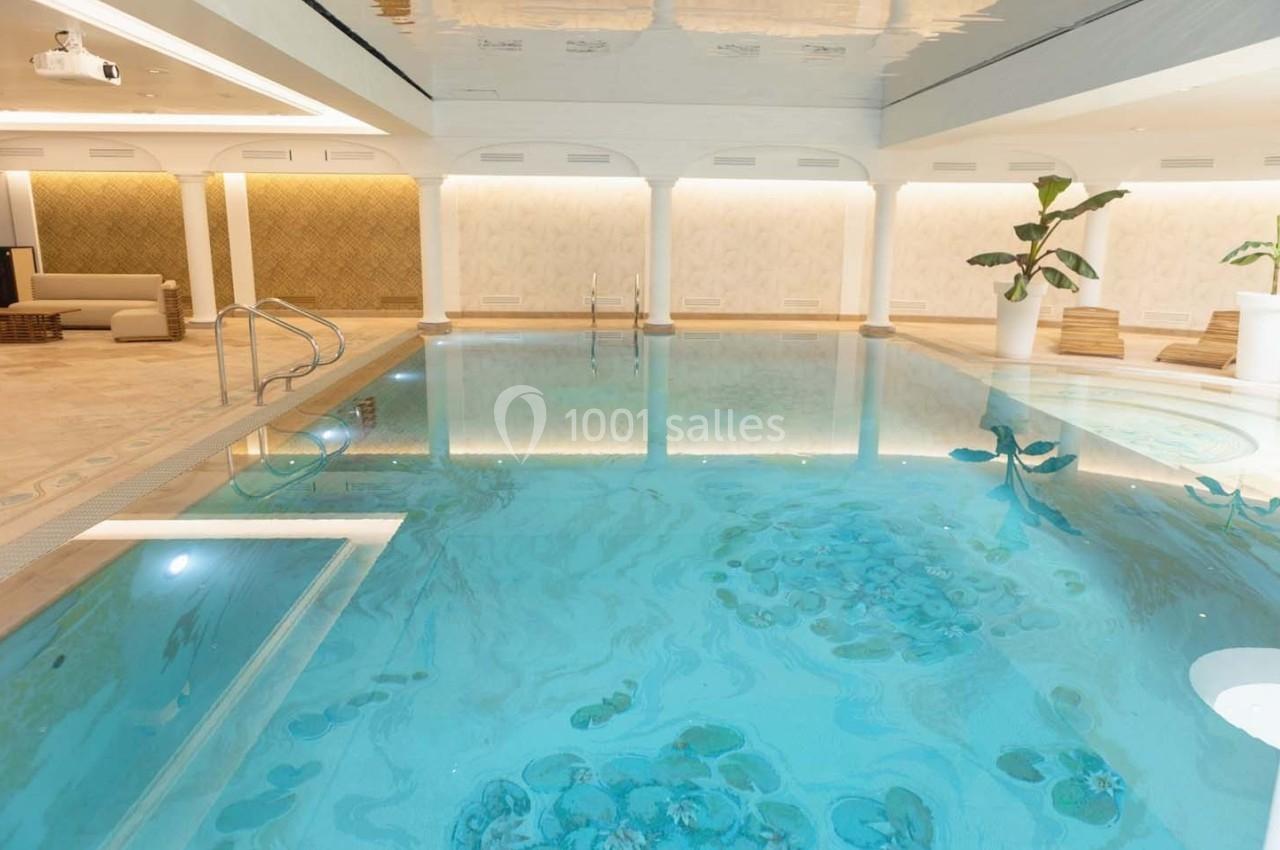 Piscine intérieure lumineuse avec eau claire, entourée de murs décoratifs, plantes et mobilier de détente.
