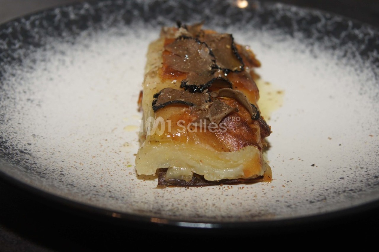 Part de gratin de pommes de terre garnie de fines tranches de truffe, servie dans une assiette sombre.