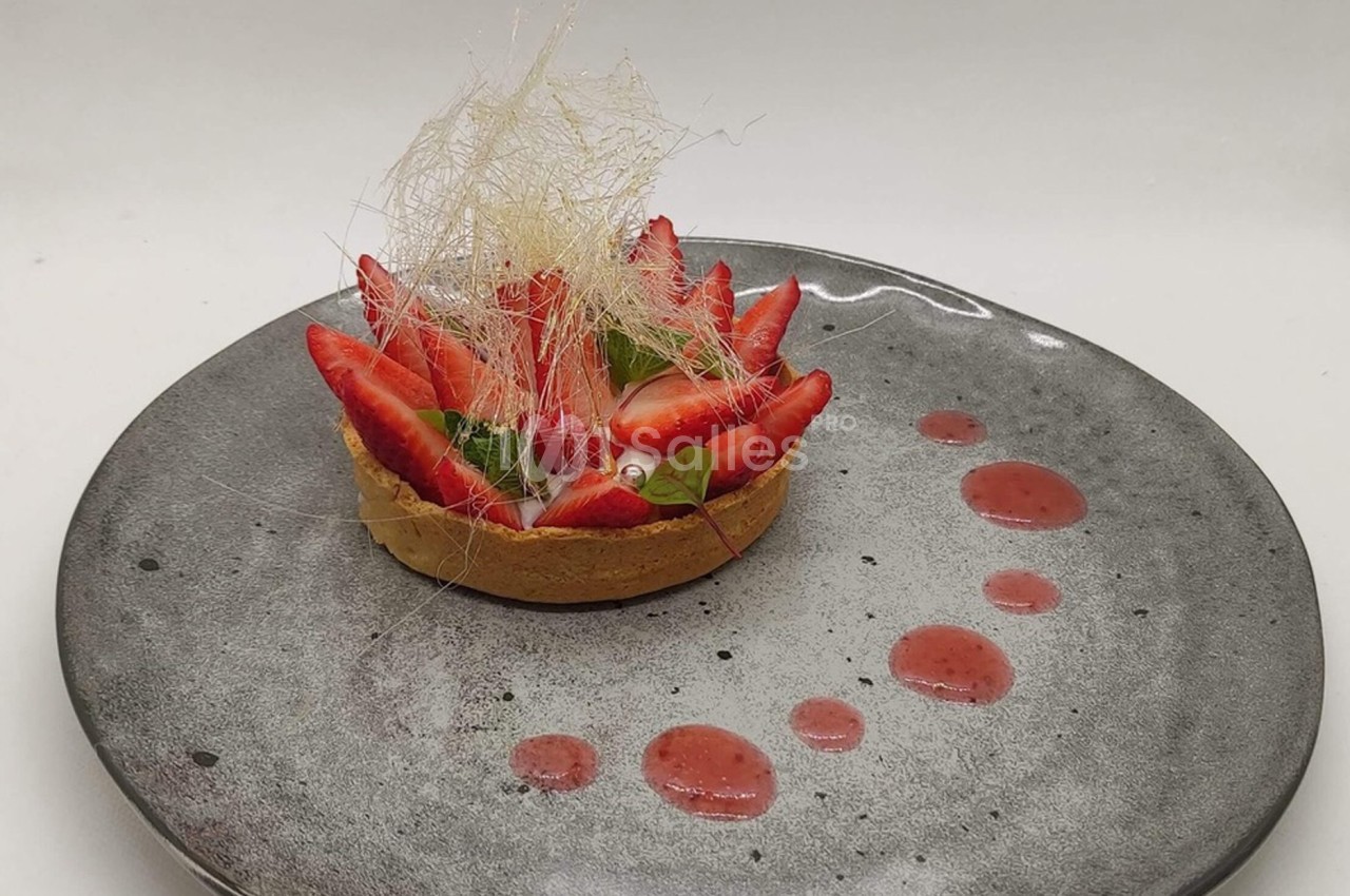 Tartelette garnie de fraises fraîches, décorée de filaments de sucre et accompagnée de points de coulis rouge.