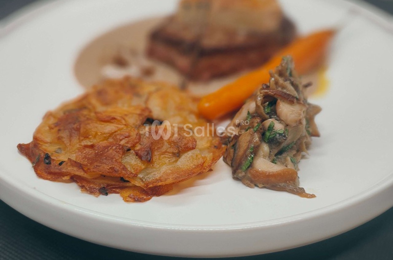 Assiette contenant une galette de pommes de terre, des champignons sautés, une carotte et une pièce de viande avec sauce.