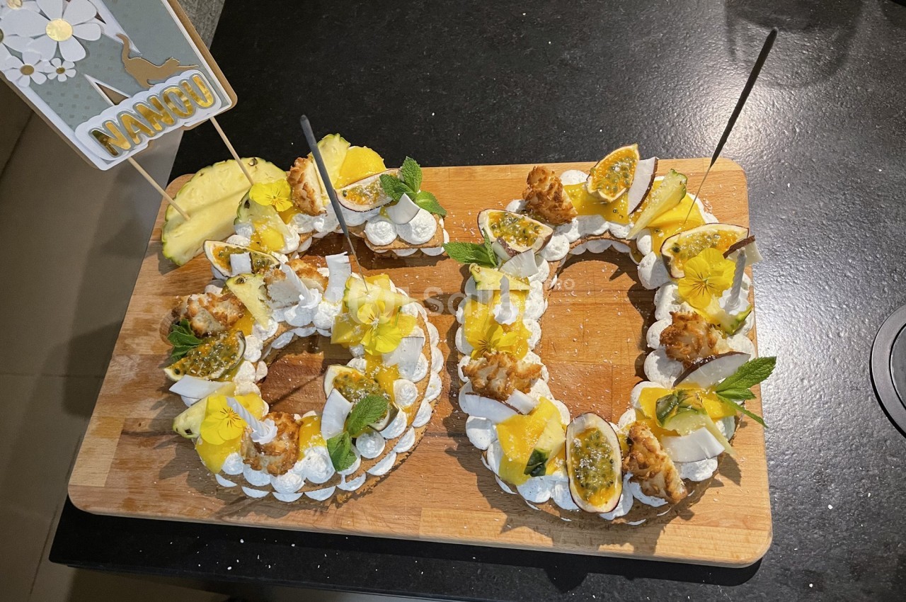 Couronnes de meringue garnies de fruits tropicaux, fleurs comestibles et décorations sur une planche en bois.