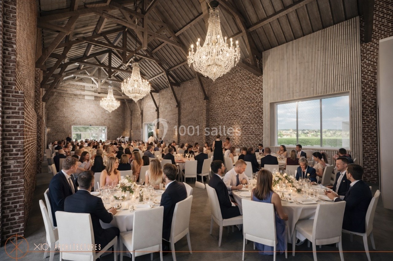 Salle de réception avec des invités assis à des tables décorées, sous des lustres en cristal et un plafond en bois.