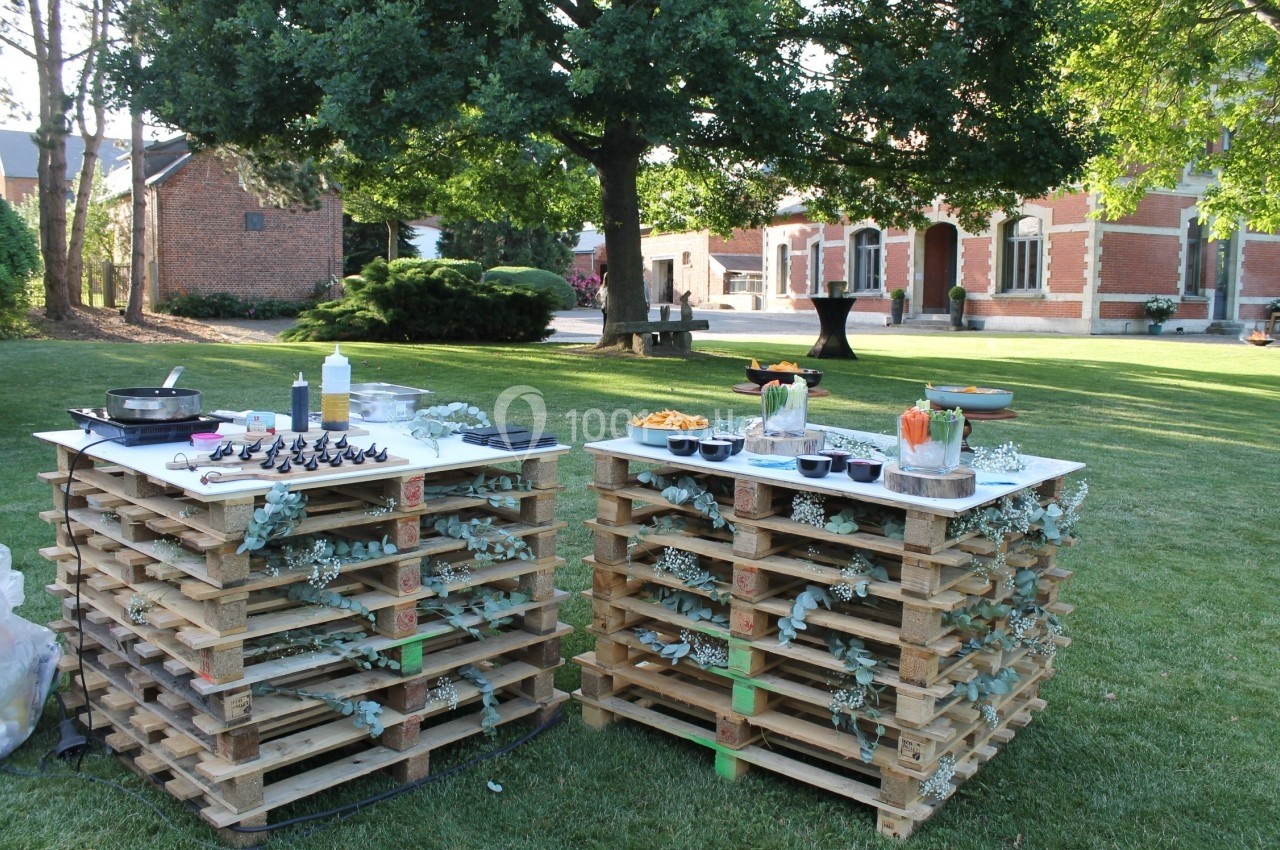 Tables en palettes décorées de feuillage, disposées dans un jardin pour un buffet en plein air.