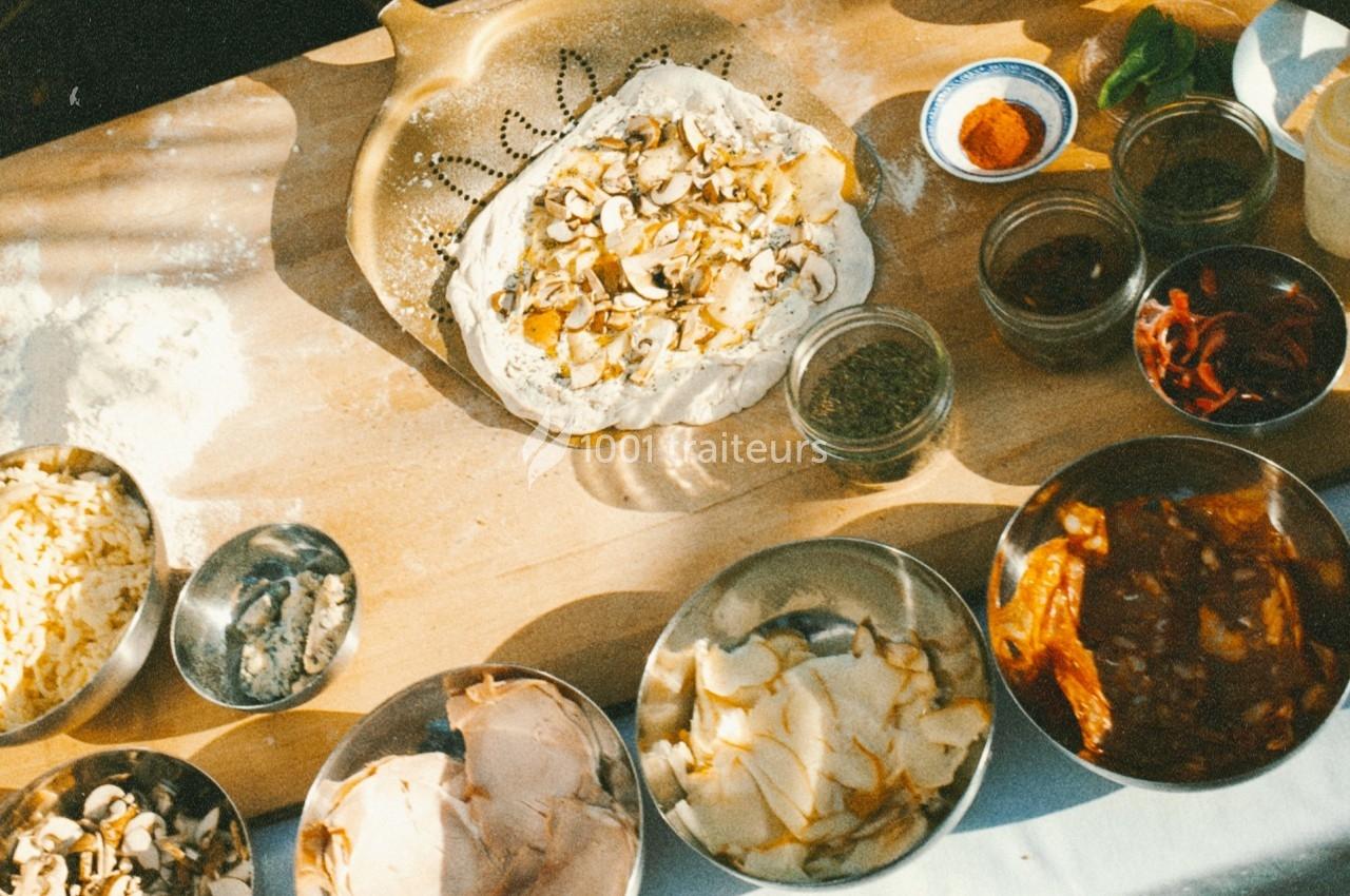 Ingrédients variés et pâte à pizza garnie de champignons disposés sur une table en bois.