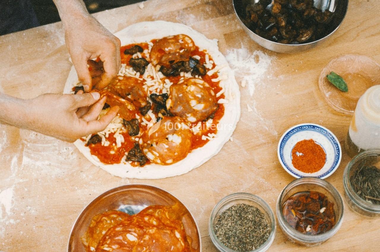 Préparation d'une pizza avec des tranches de chorizo, sauce tomate et garnitures variées sur un plan de travail en bois.