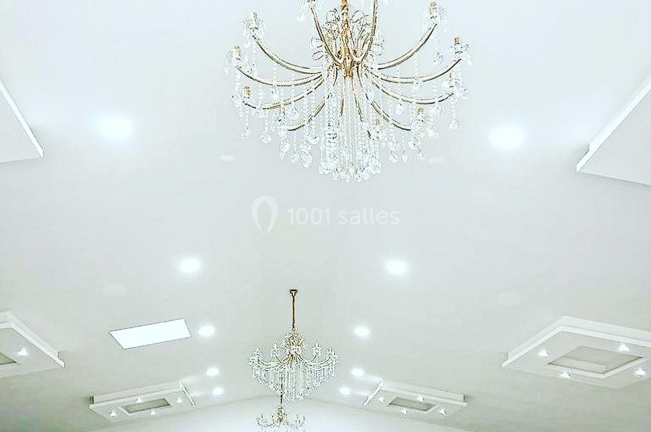 Salle spacieuse avec plafond blanc, lustres en cristal suspendus et murs ornés de moulures.
