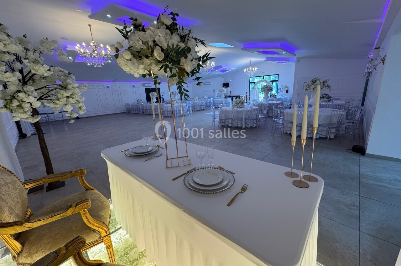 Salle de réception décorée avec des tables dressées, des chandeliers, des fleurs blanches et un éclairage LED violet.