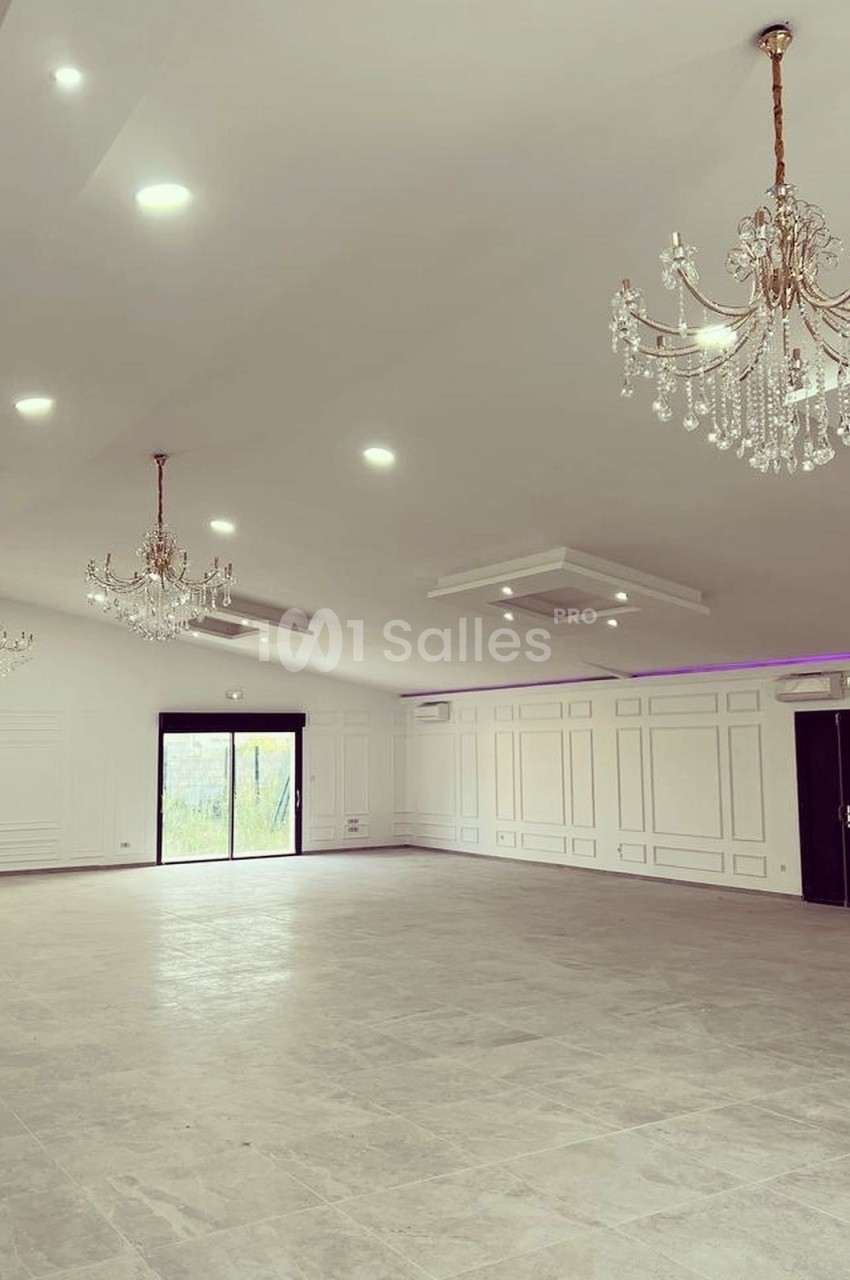 Salle spacieuse avec sol en carrelage, murs blancs, lustres en cristal et éclairage moderne au plafond.