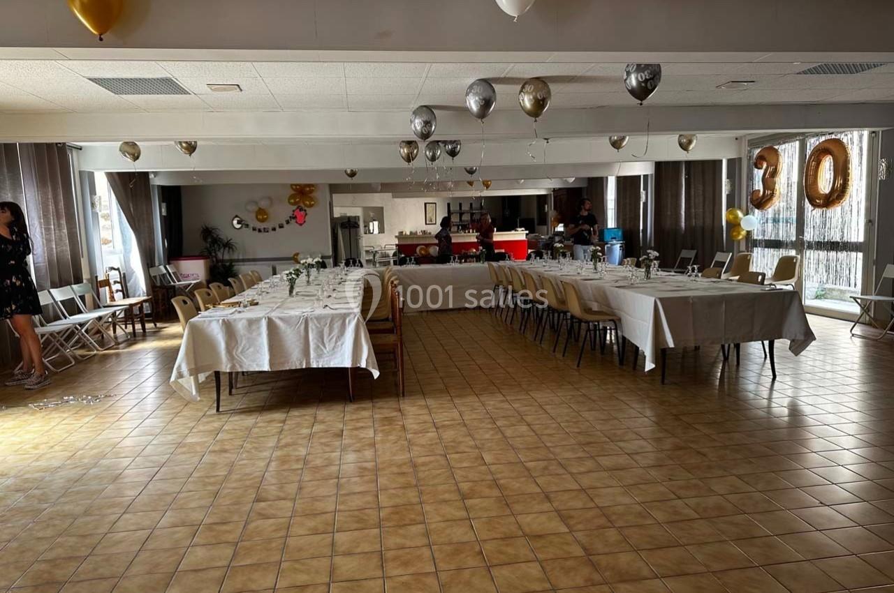 Salle décorée pour une fête avec tables dressées, ballons suspendus et chiffre ’30’ en ballon doré.