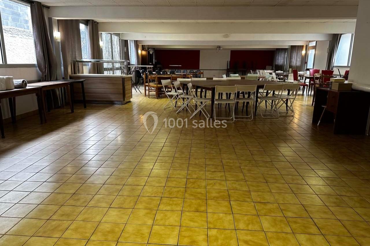 Salle spacieuse avec tables et chaises disposées, carrelage jaune au sol et grandes fenêtres laissant entrer la lumière.