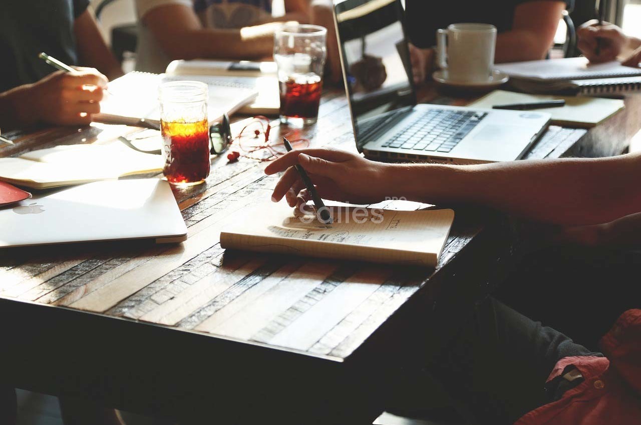 Personnes travaillant autour d'une table en bois avec ordinateurs, cahiers et boissons.