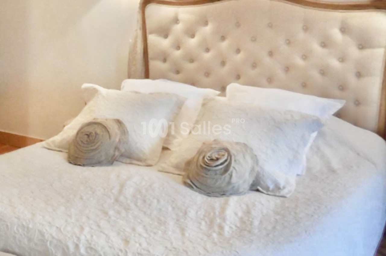 Lit double avec tête de lit capitonnée beige, draps blancs et coussins décoratifs en forme de roses.
