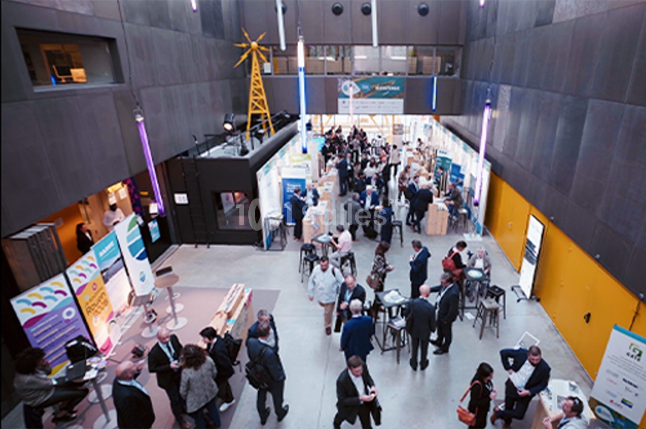 Vue plongeante sur un espace d'exposition intérieur avec des stands, des visiteurs et une ambiance professionnelle.