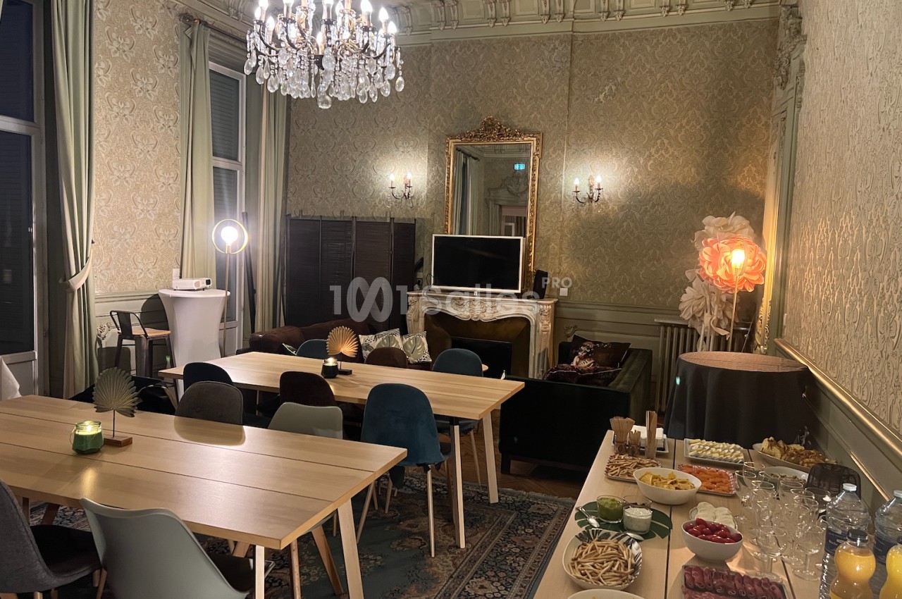 Salle élégante avec tables en bois, chaises colorées, buffet de snacks et boissons, lustre et décoration raffinée.