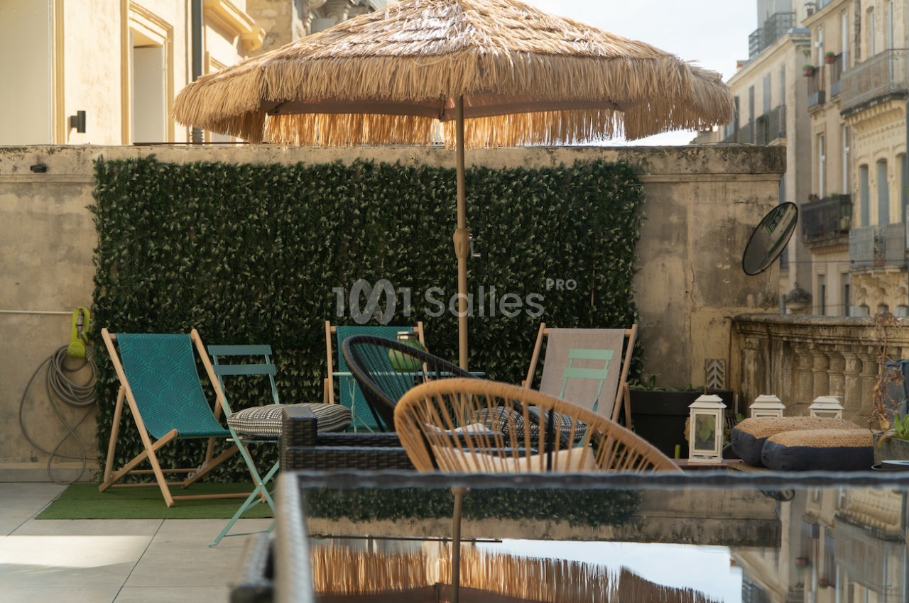 Terrasse aménagée avec des chaises, une table, un parasol en paille et un mur végétal, en milieu urbain.