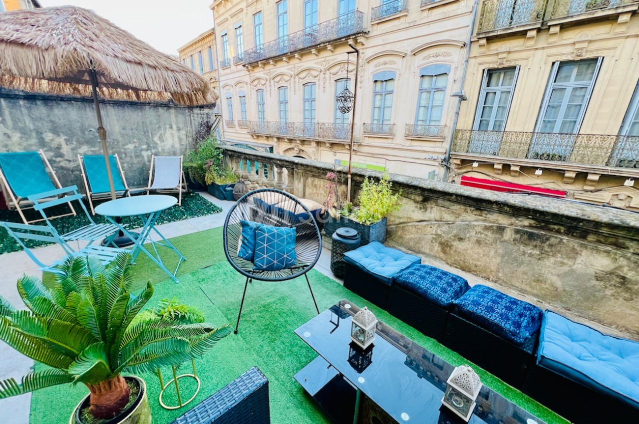Terrasse aménagée avec mobilier de jardin, pelouse artificielle, plantes et vue sur des façades anciennes en pierre.