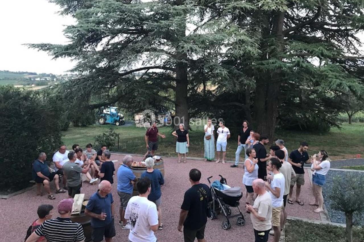 Groupe de personnes rassemblées en plein air sous des arbres, discutant et partageant un moment convivial.
