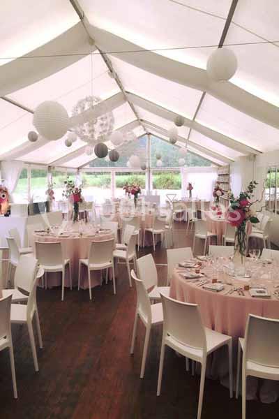 Salle de réception sous chapiteau avec tables rondes dressées, décorations florales et lanternes suspendues.