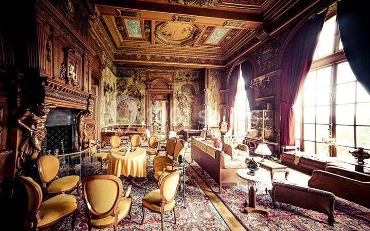 Salle richement décorée avec boiseries sculptées, fresques murales, mobilier ancien et grandes fenêtres laissant entrer la…