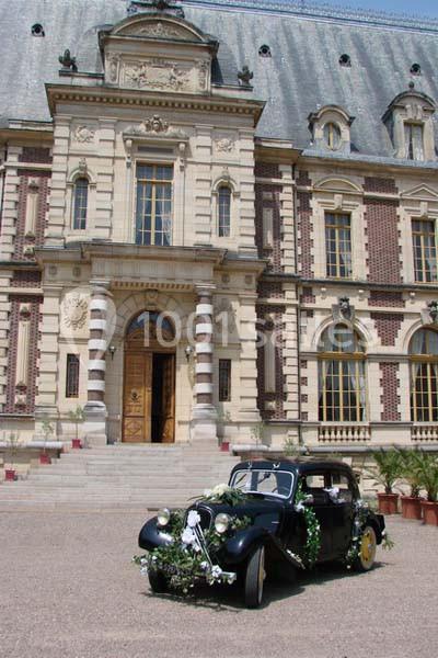 Voiture ancienne décorée de fleurs garée devant un bâtiment historique en pierre et briques rouges.