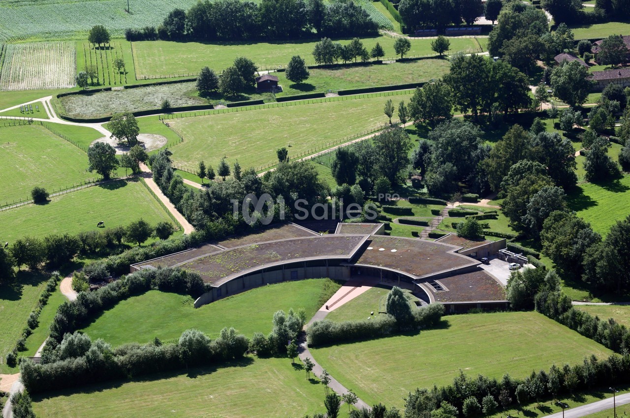Vue aérienne d'un bâtiment moderne en forme d'étoile avec un toit végétalisé, entouré de champs et d'arbres.