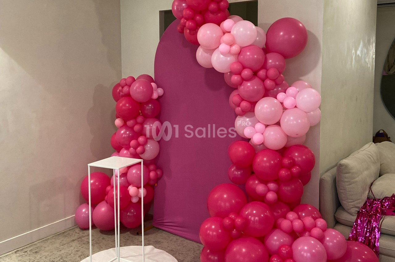 Décoration composée d'arche de ballons roses et fuchsia autour d'un fond rose, avec un support blanc au premier plan.
