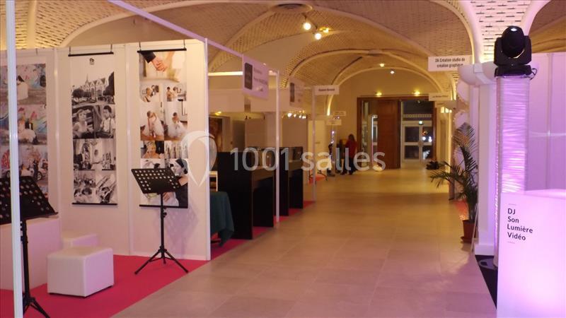 Un couloir d'exposition avec stands éclairés, affiches, et équipements audio sous un plafond voûté en bois.