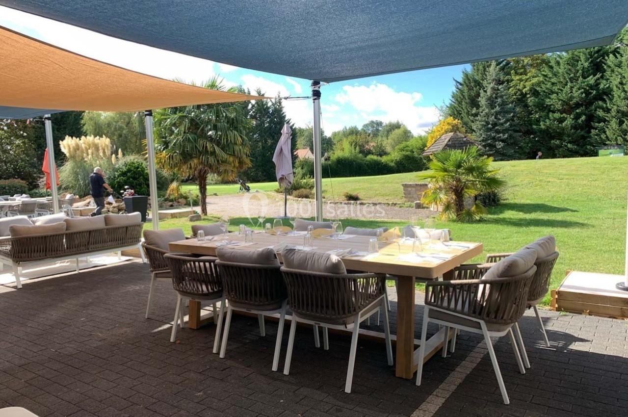 Terrasse aménagée avec une grande table en bois, des chaises confortables et des voiles d'ombrage, donnant sur un jardin…