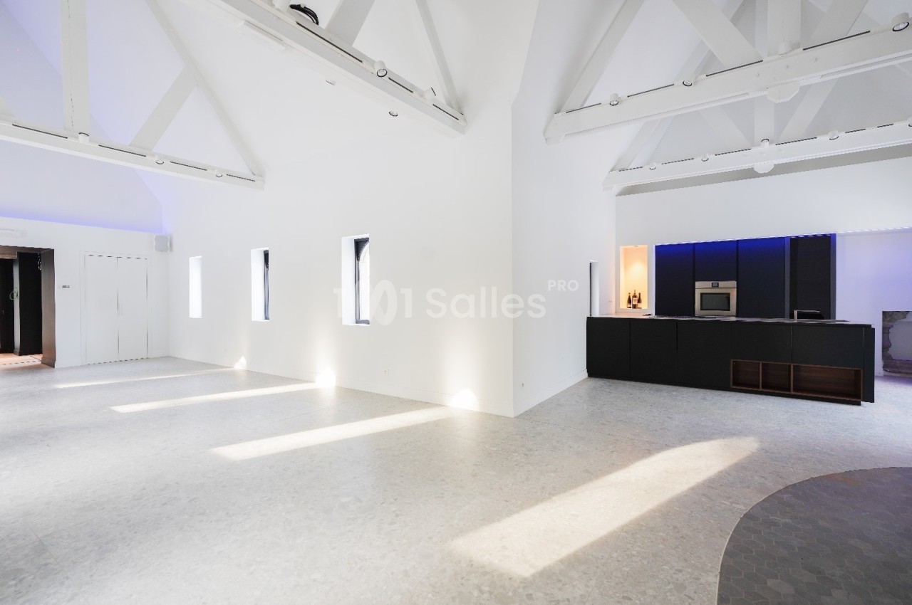 Intérieur lumineux avec murs blancs, plafond à poutres apparentes et cuisine moderne noire éclairée par des LED.